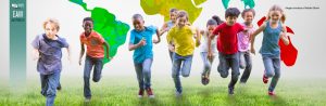 A group of kids is running on the grass; behind them is a colorful mural of the world map.