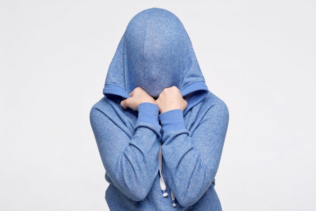 A teenager is pulling a blue hoodie over his/hers head looking stresses. 
