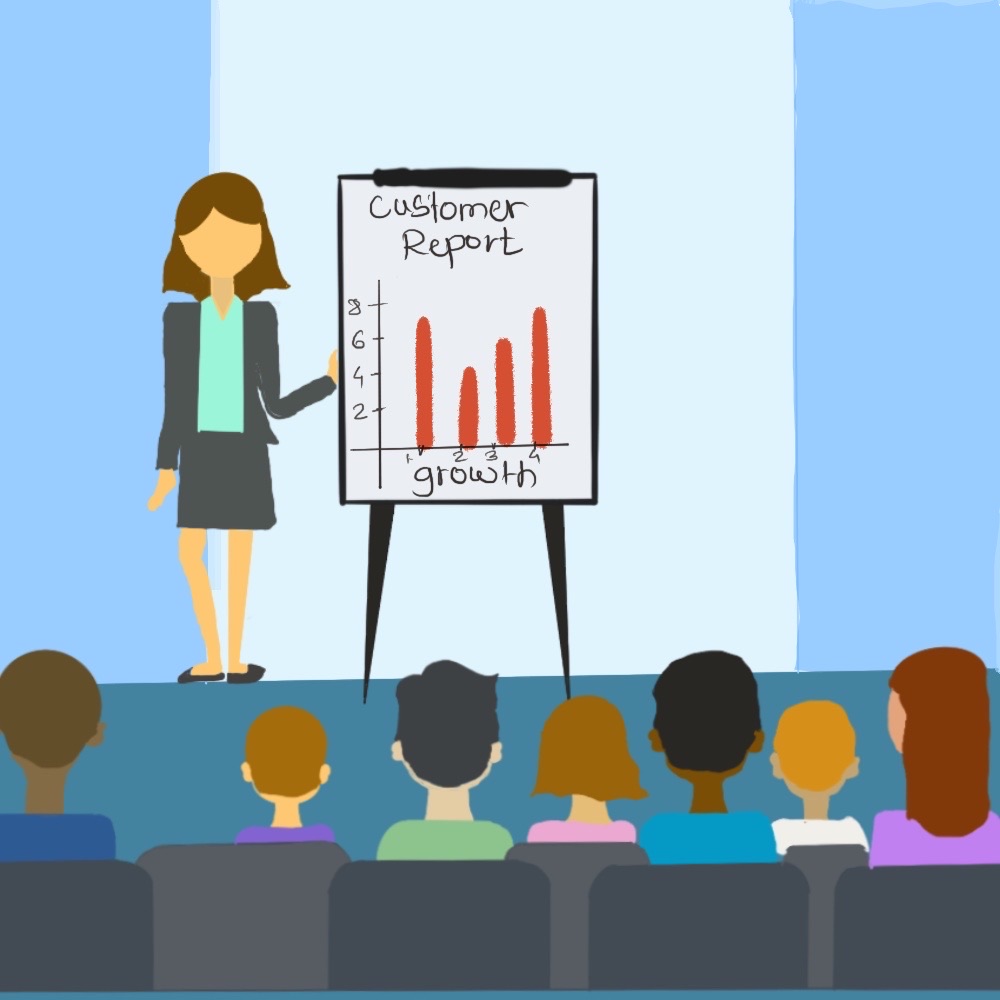 A female presenter stands next to a board with graph data and talks to a room of people.