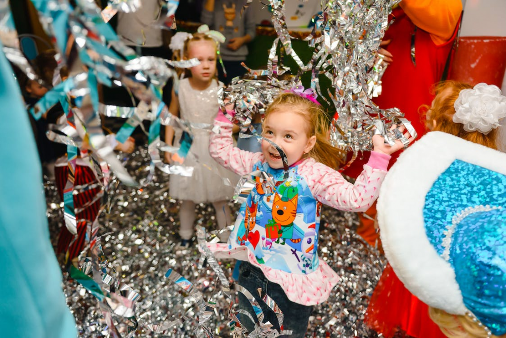 A young girl is standing in the middle of the room, decorated in glittery party décor, surrounded by her family and friends. 