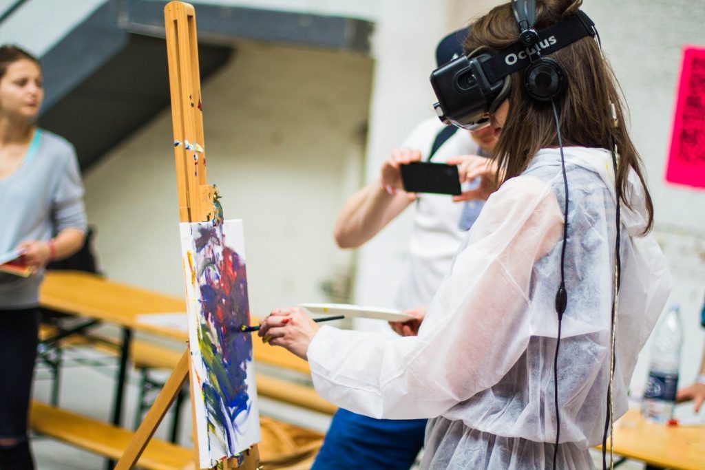 Young female is painting on the canvas while using virtual reality set. 