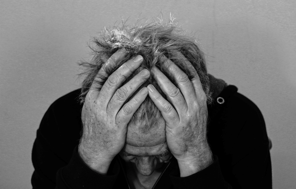 Black and white picture of a man stroking his hands through his hair looking desperate. 