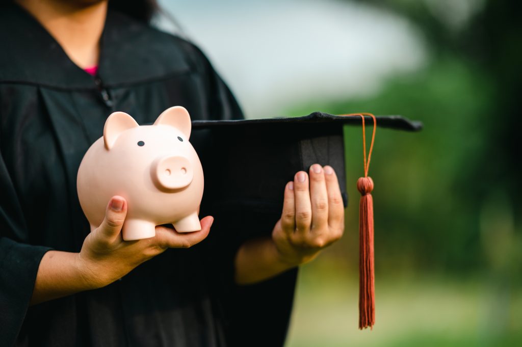 A female college graduate is holding a piggy bank in her hands.