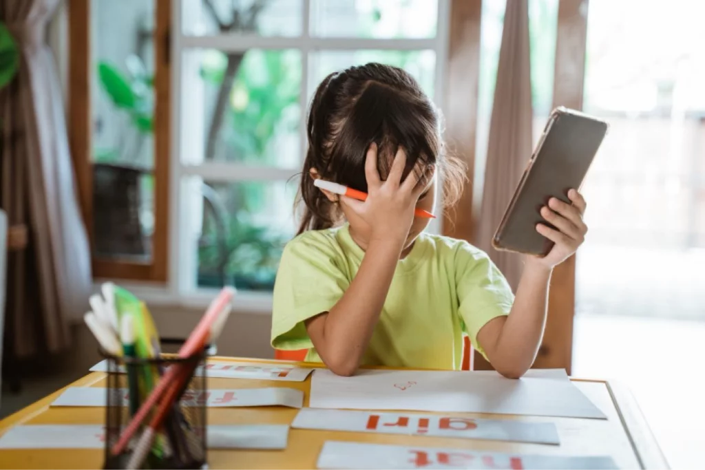 her desk covering her face with right hand while holding a phone in her left hand.