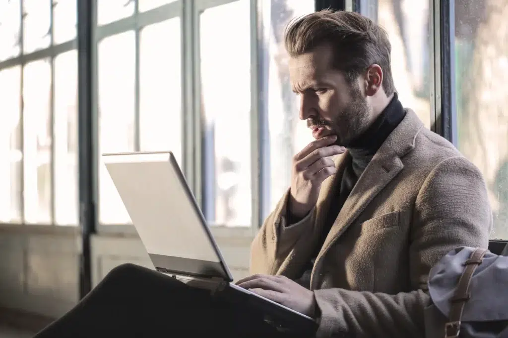 white male dressed in business casual sits with his laptop and reads something from the screen