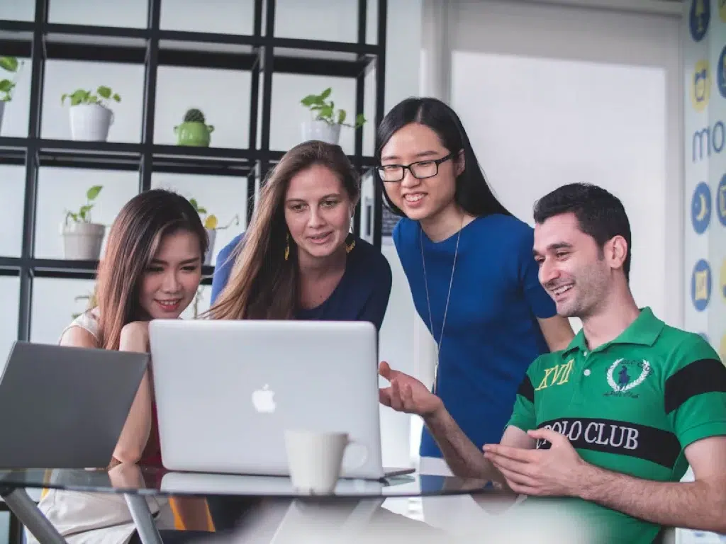 a group of young diverse people stands around the laptop - laughing at something on the screen