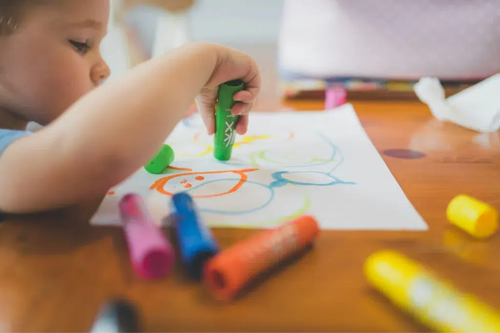 young child drawing on a piece paper with colorful markers