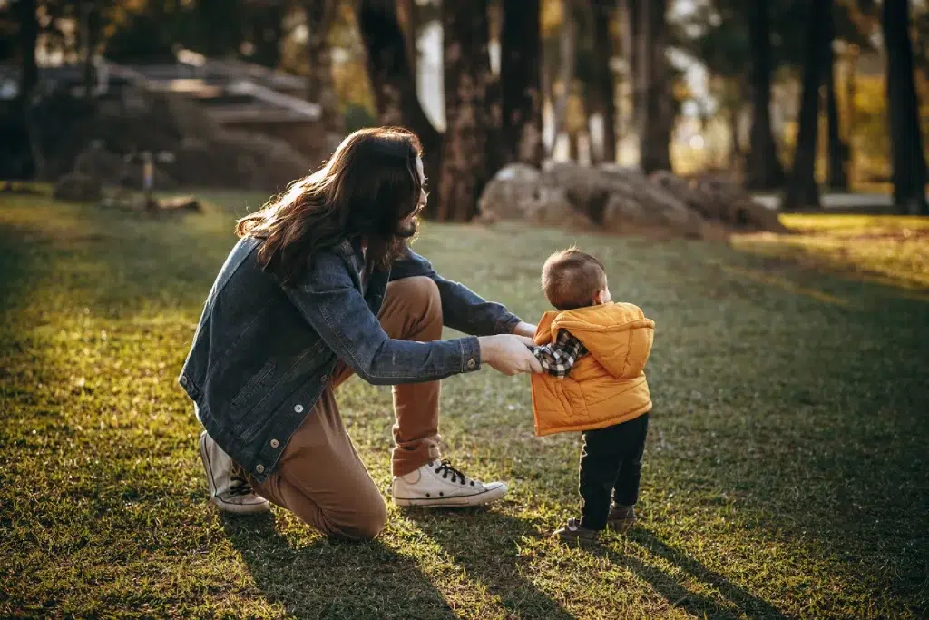 young female is holding a toddler while he stands in the greenery - playful moment
