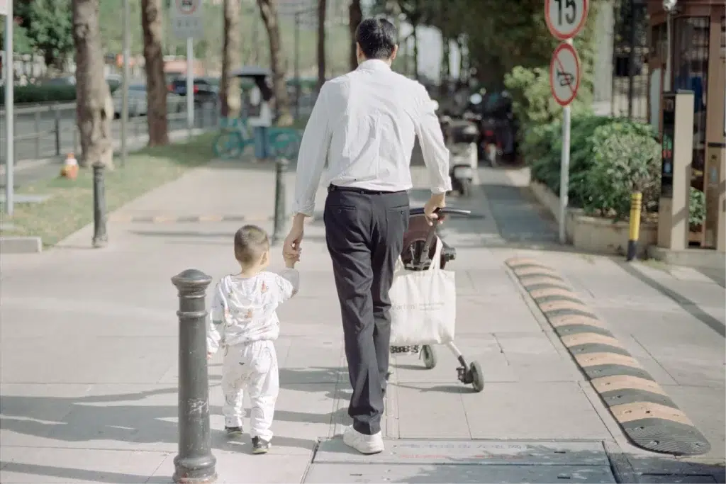 Man walks on the walkway while holding toddler's hand.