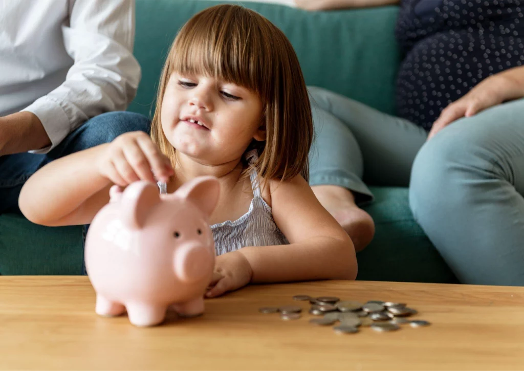 a fair-haired girl is placing coins into piggy bank