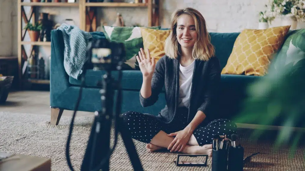 young female sitting on the ground in front of the sofa recording a video of herself