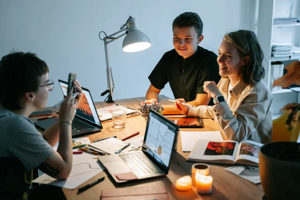 a group of young people sitting around the table working on a project.