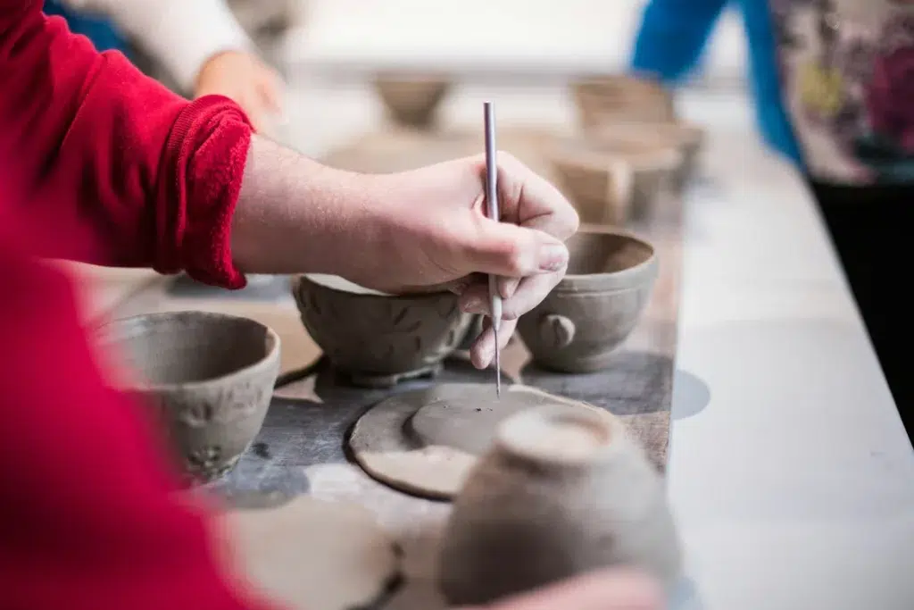 zoomed in image shows a person working on a clay pottery item.