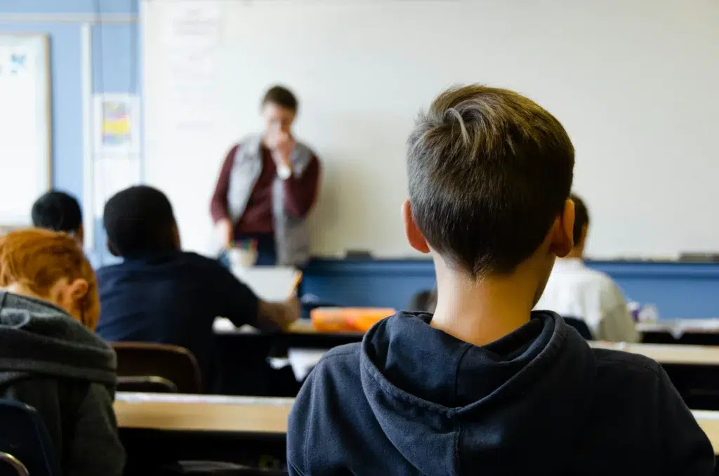 group of students are listening to their male teacher who stands in front of the white board