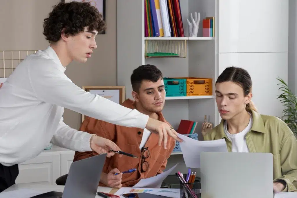 photo depicts three young males sitting around the desk and looking at a document.