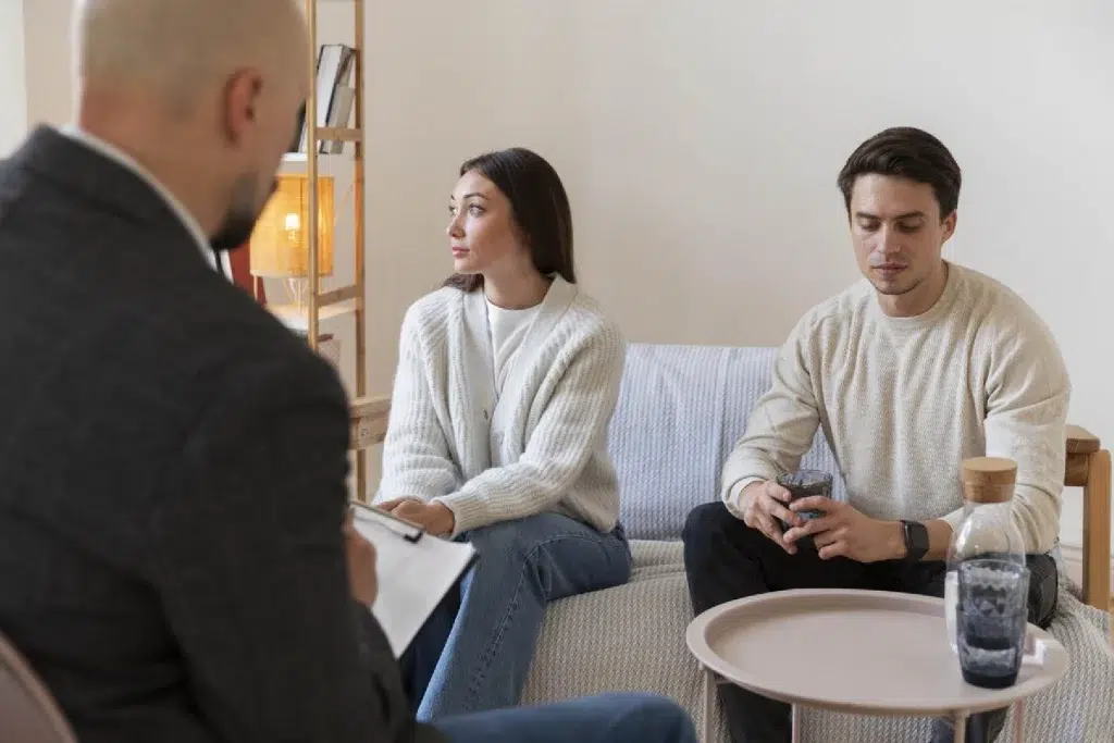 Two young people, looking sad, are sitting on the sofa in the therapist office.