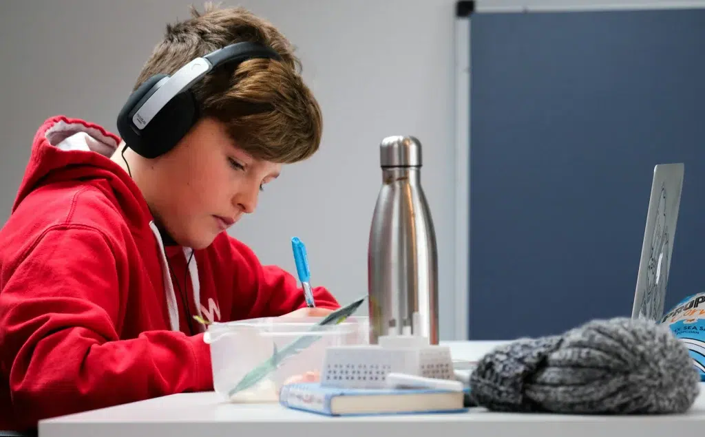 woman in red and white hoodie wearing black headphones studying at the desk