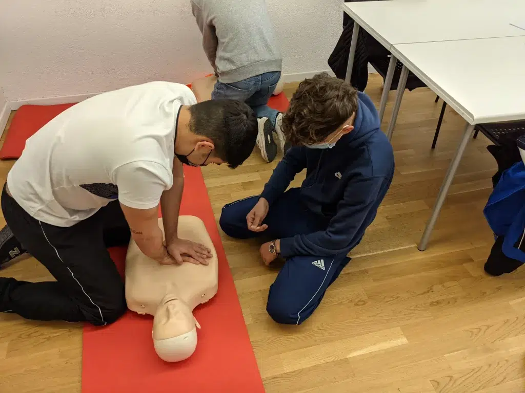 man in white t-shirt and blue pants is performs CPR on a dummy on the floor