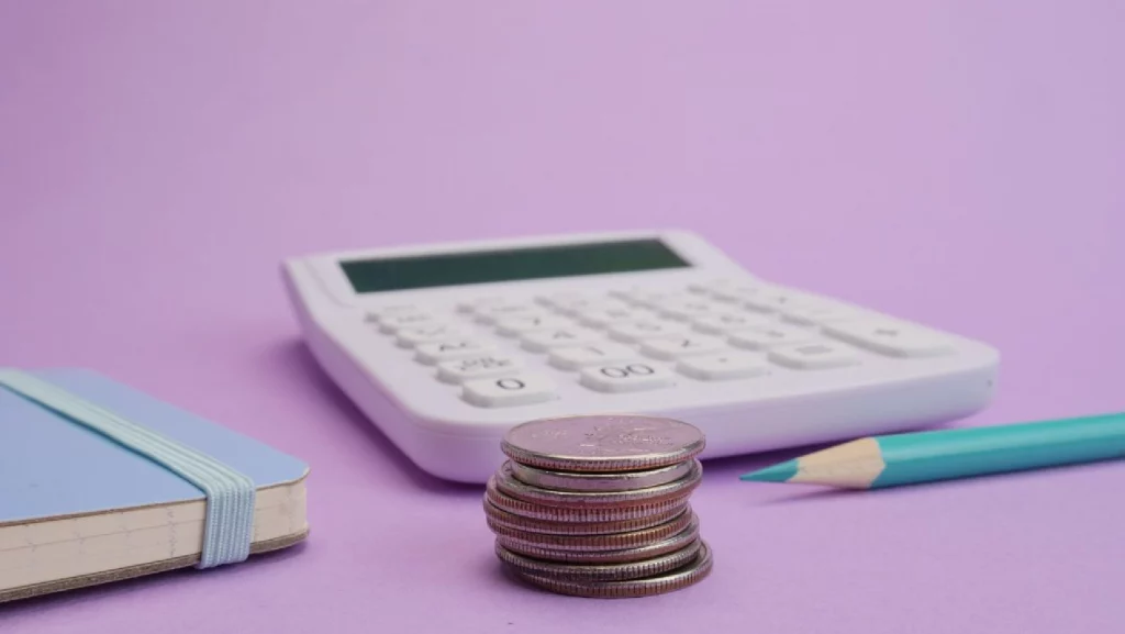 a calculator and a small pile of coins on a pastel pink background
