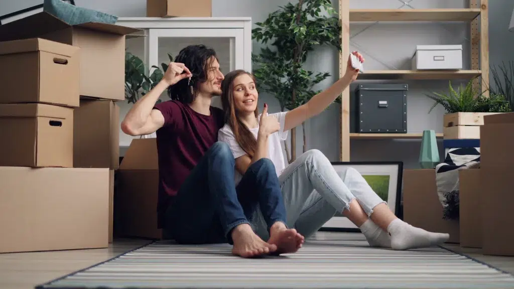 young couple taking a selfie sitting on the floor surrounded by moving boxes