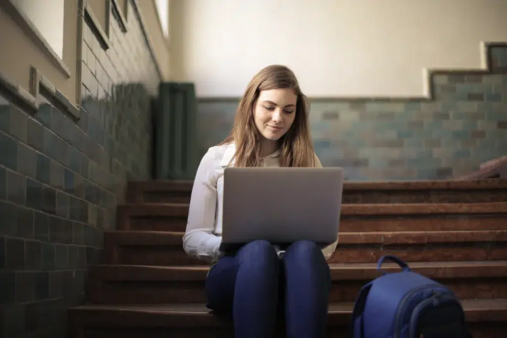 Young woman sitting on stairs using laptop for remote work. Perfect for promoting digital nomad lifestyle.