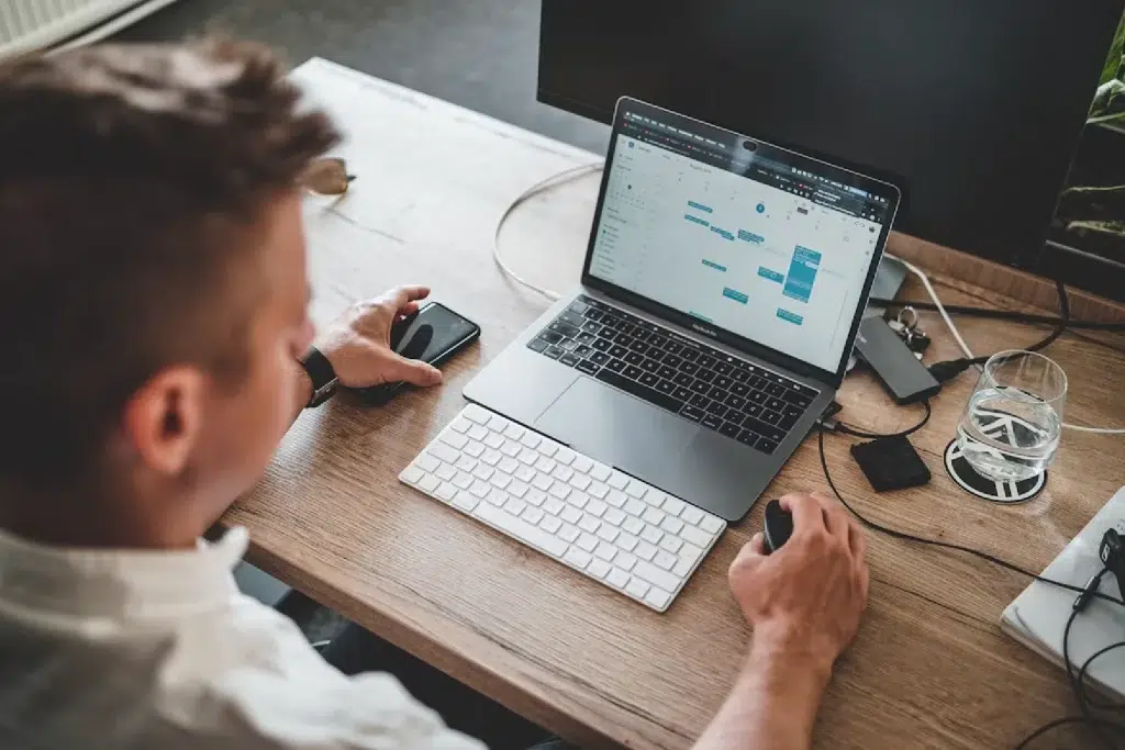 man holding a mouse and iPhone while using a MacBook Pro
