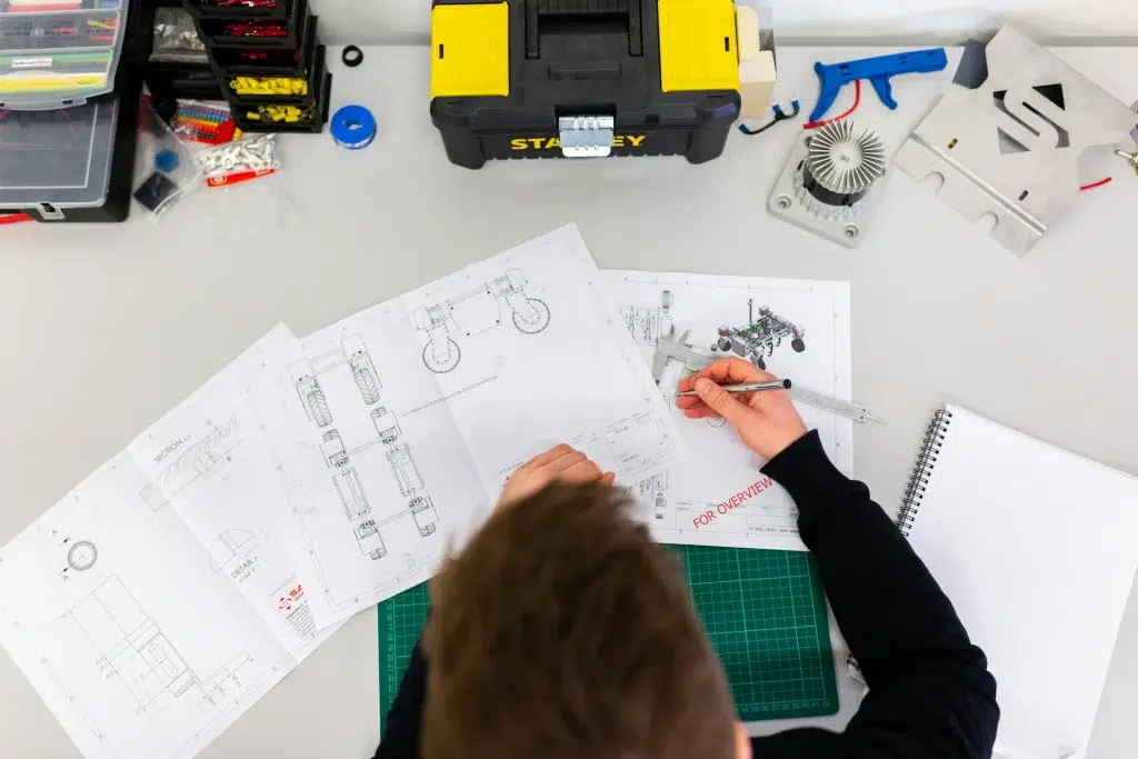 A person using a caliper to measure technical engineering drawings on a desk